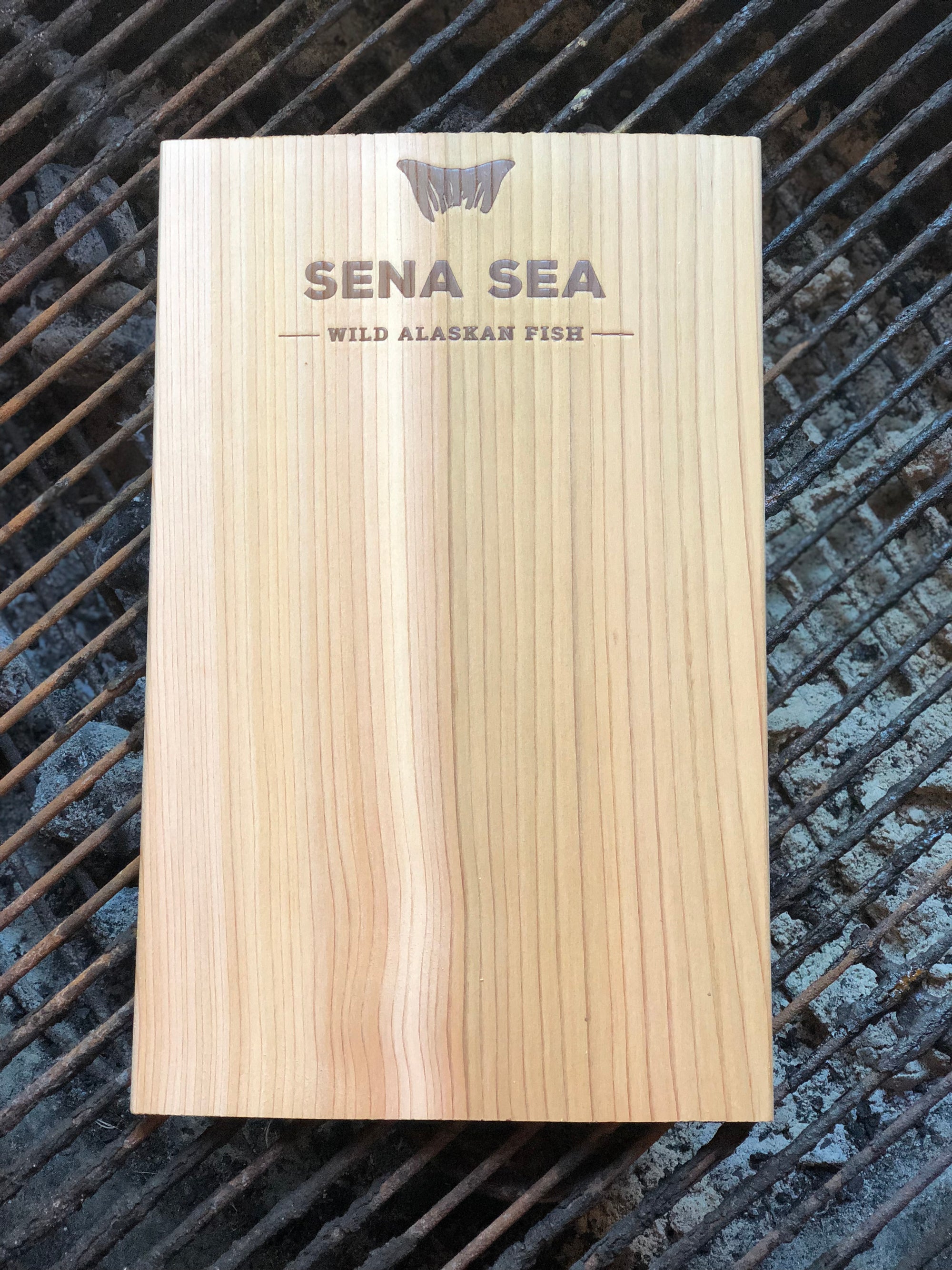 cedar grilling plank with 'Sena Sea' branding on a grill surface