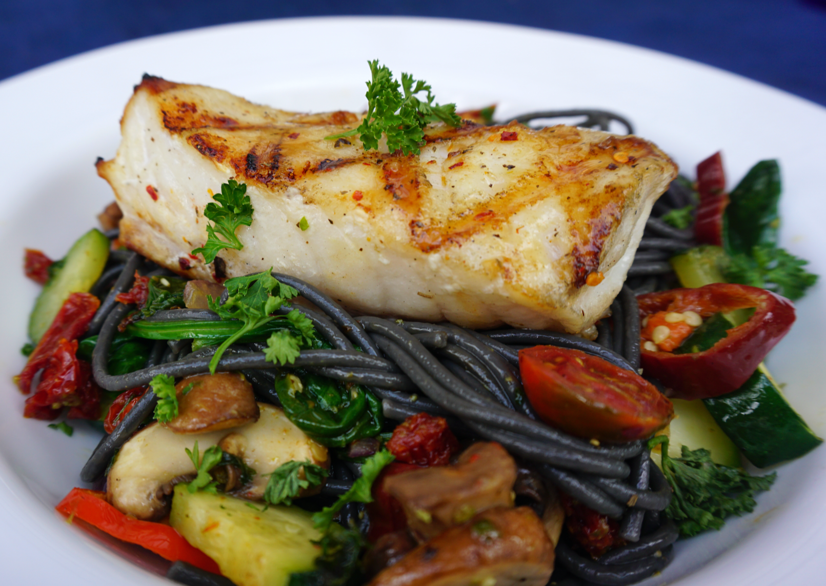 Wild caught Alaskan rockfish fillet on a bed of black noodles and veg