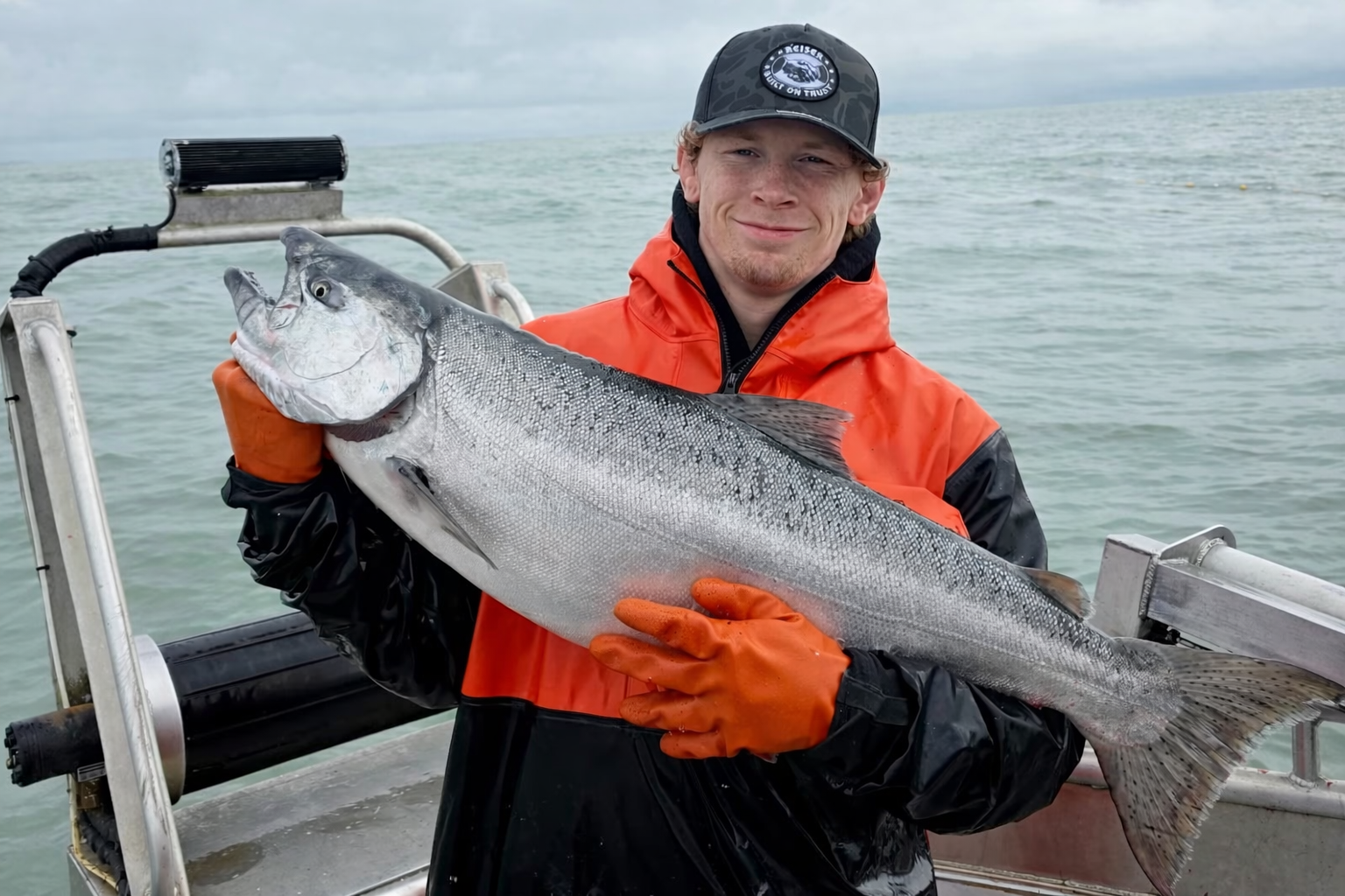 fisherman holding a large fish on a boat with water in the background