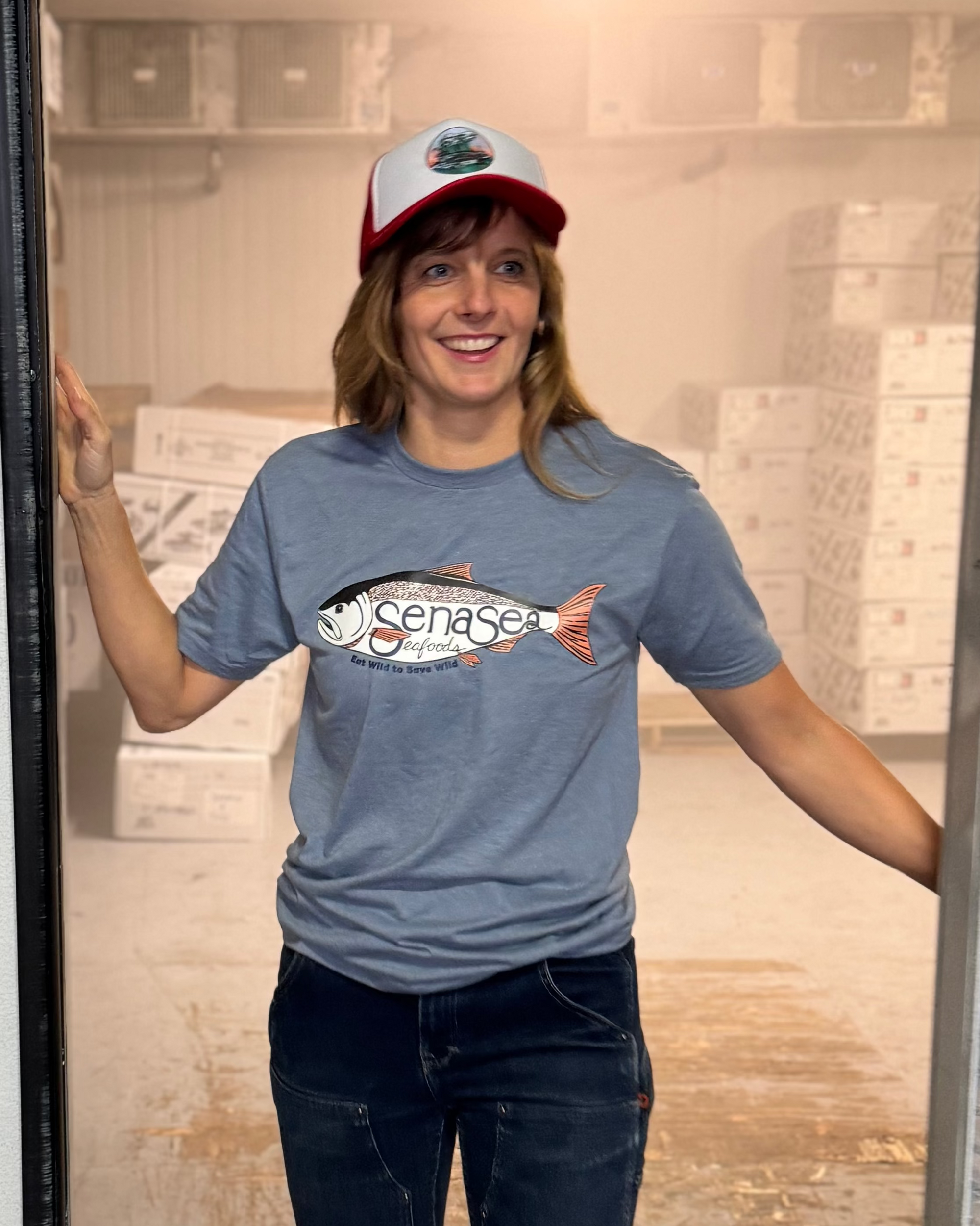Person wearing a blue t-shirt with a fish graphic, standing inside a large metal door.