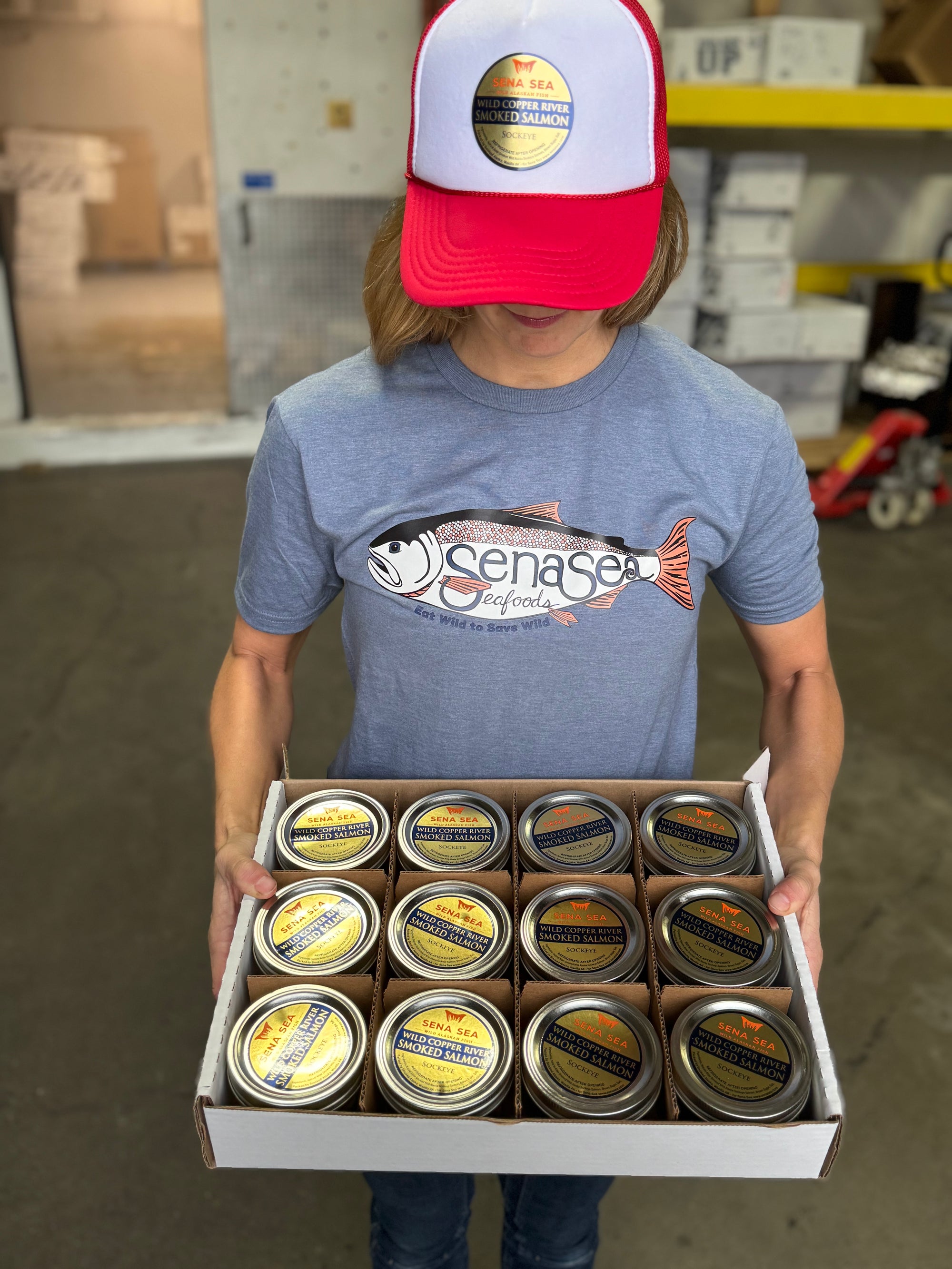 Person holding a box of Senas canned fish in a warehouse setting
