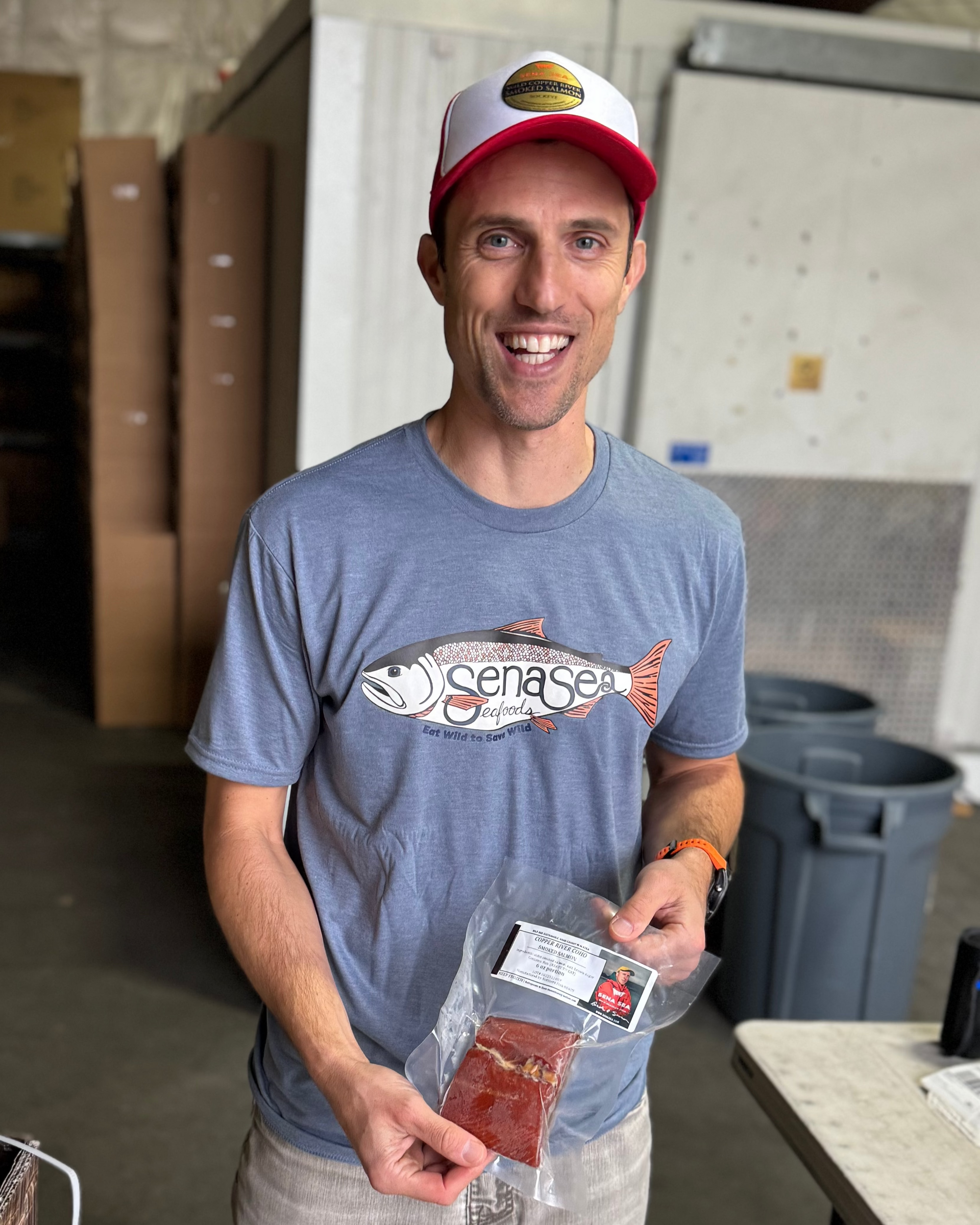 Man holding packaged salmon and wearing a fish shirt in a warehouse setting