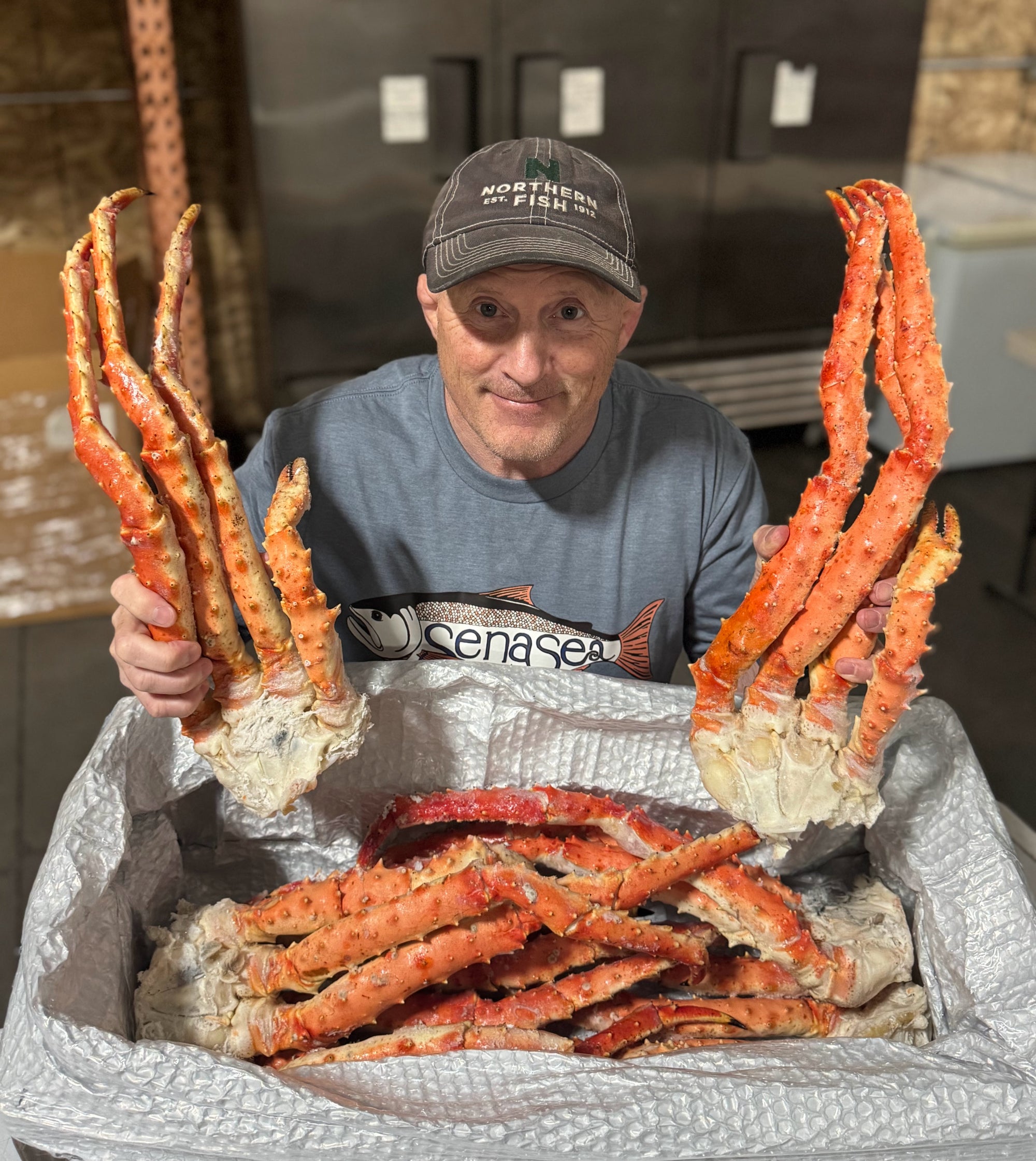 Rich holding extra large red king crab legs with a sena sea shirt in a warehouse