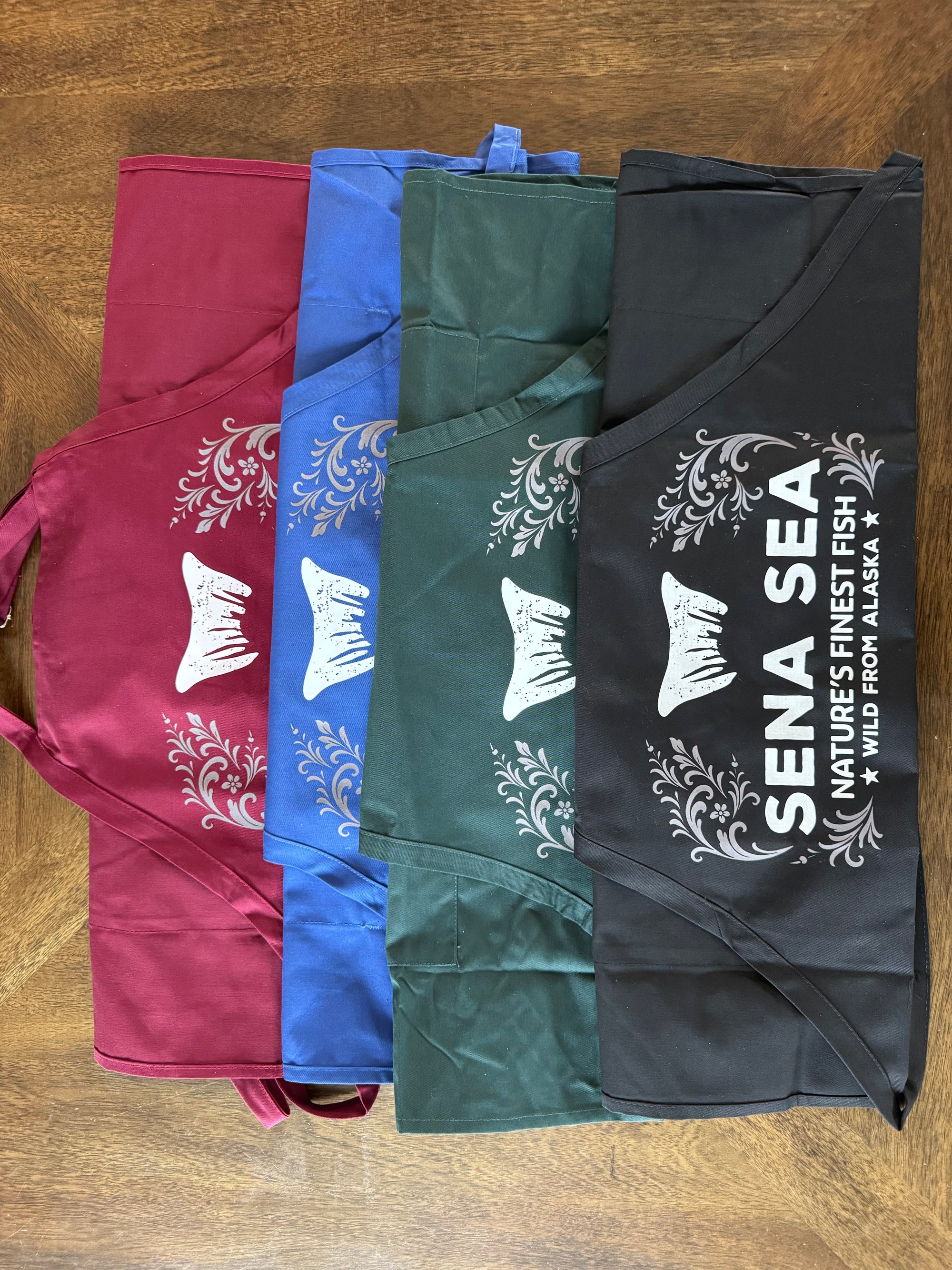 Four folded aprons in different colors with a brand logo on a wooden surface