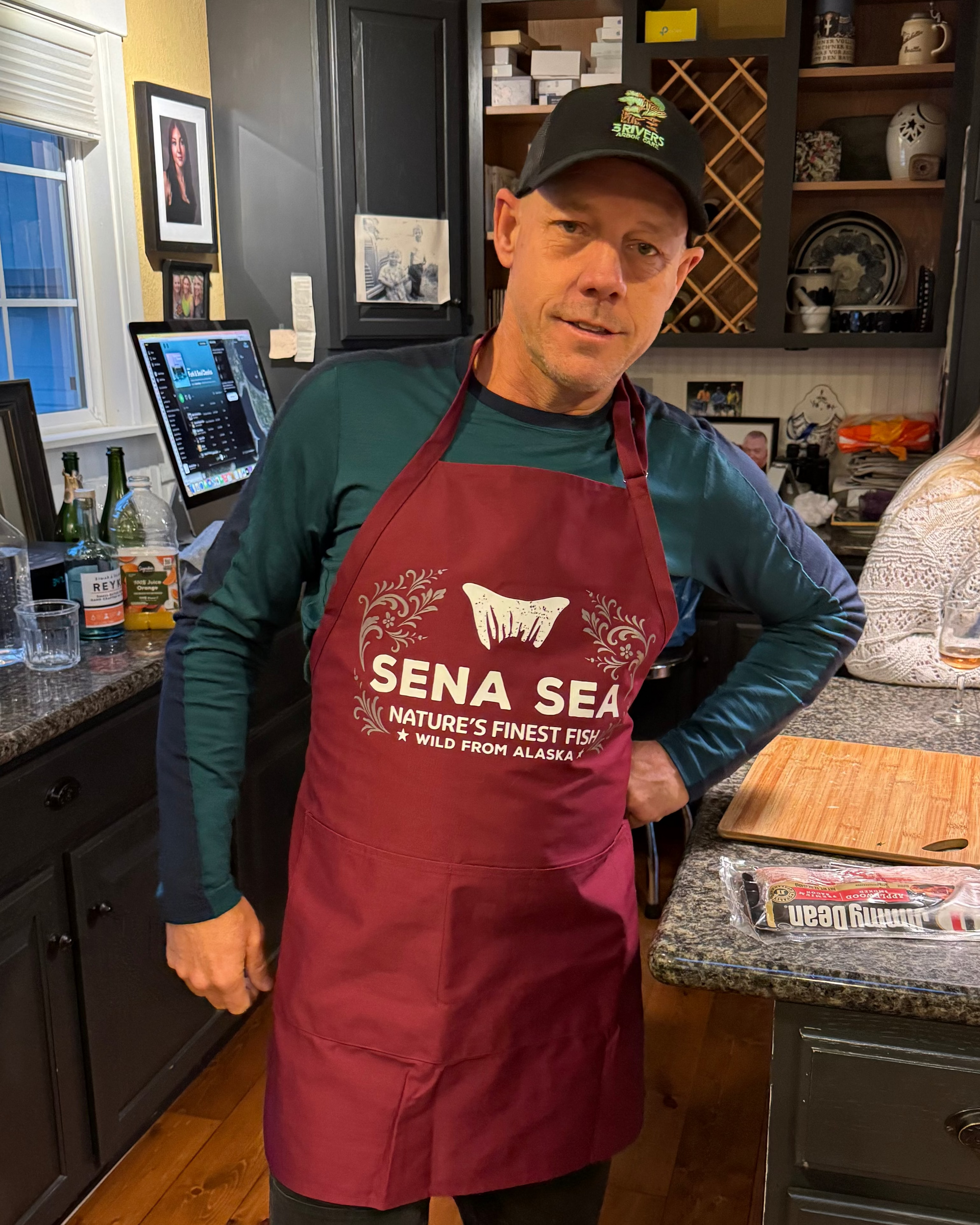 Man wearing a red apron with 'Sena Sea' branding in a kitchen setting.