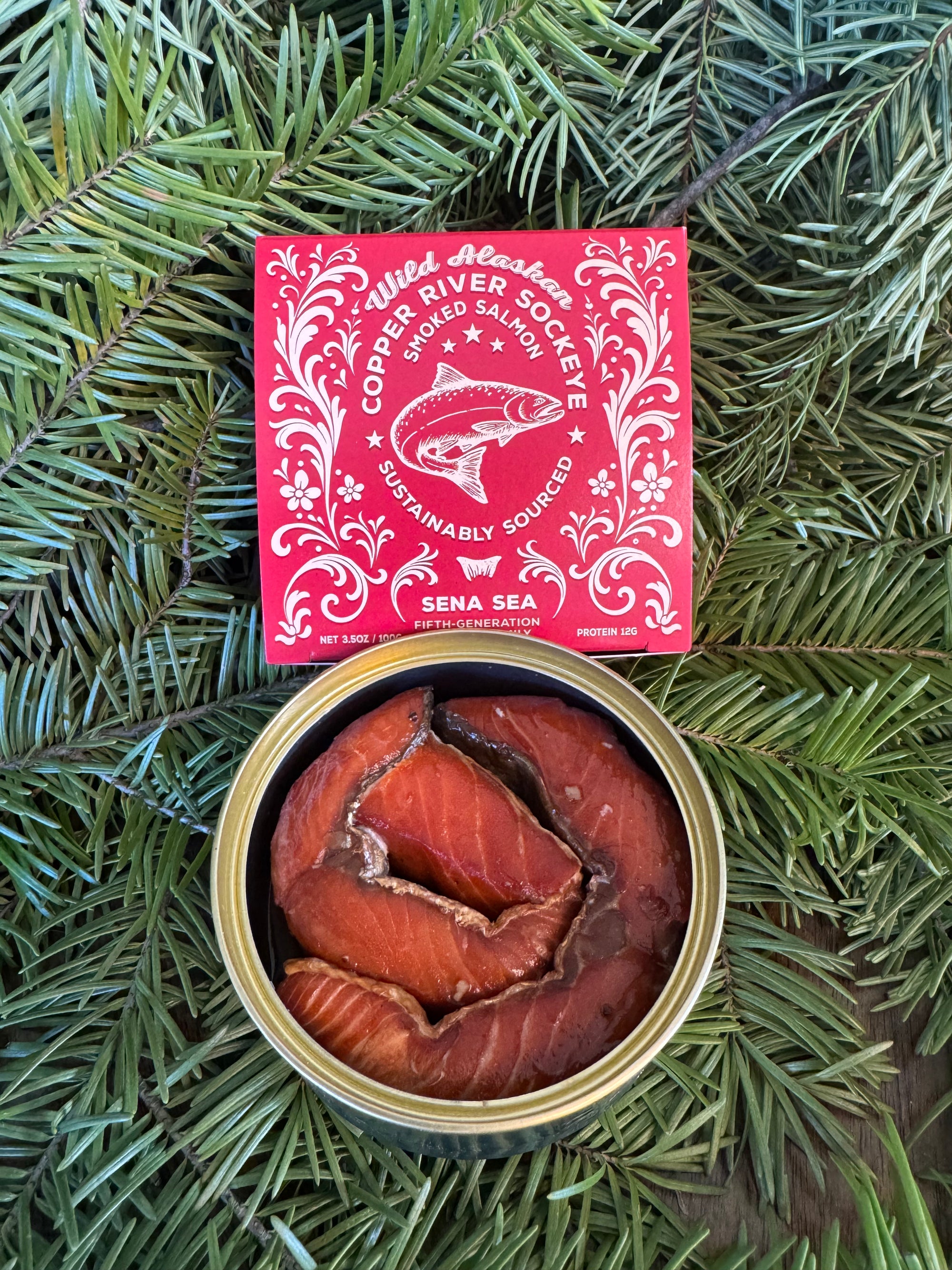 Canned smoked Copper River sockeye salmon with a red label on green foliage