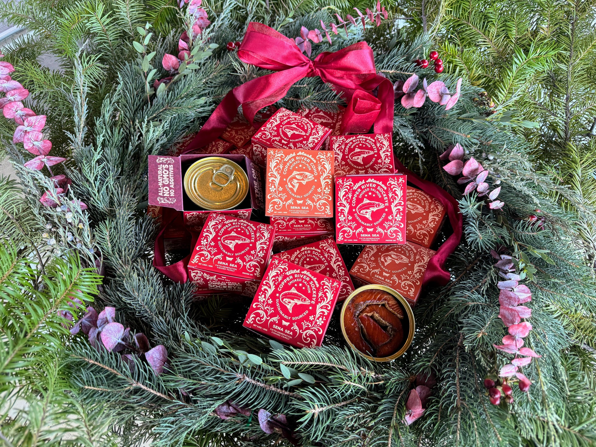 Decorative wreath with red boxes of smoked Copper River sockeye and ribbons on a green leafy background