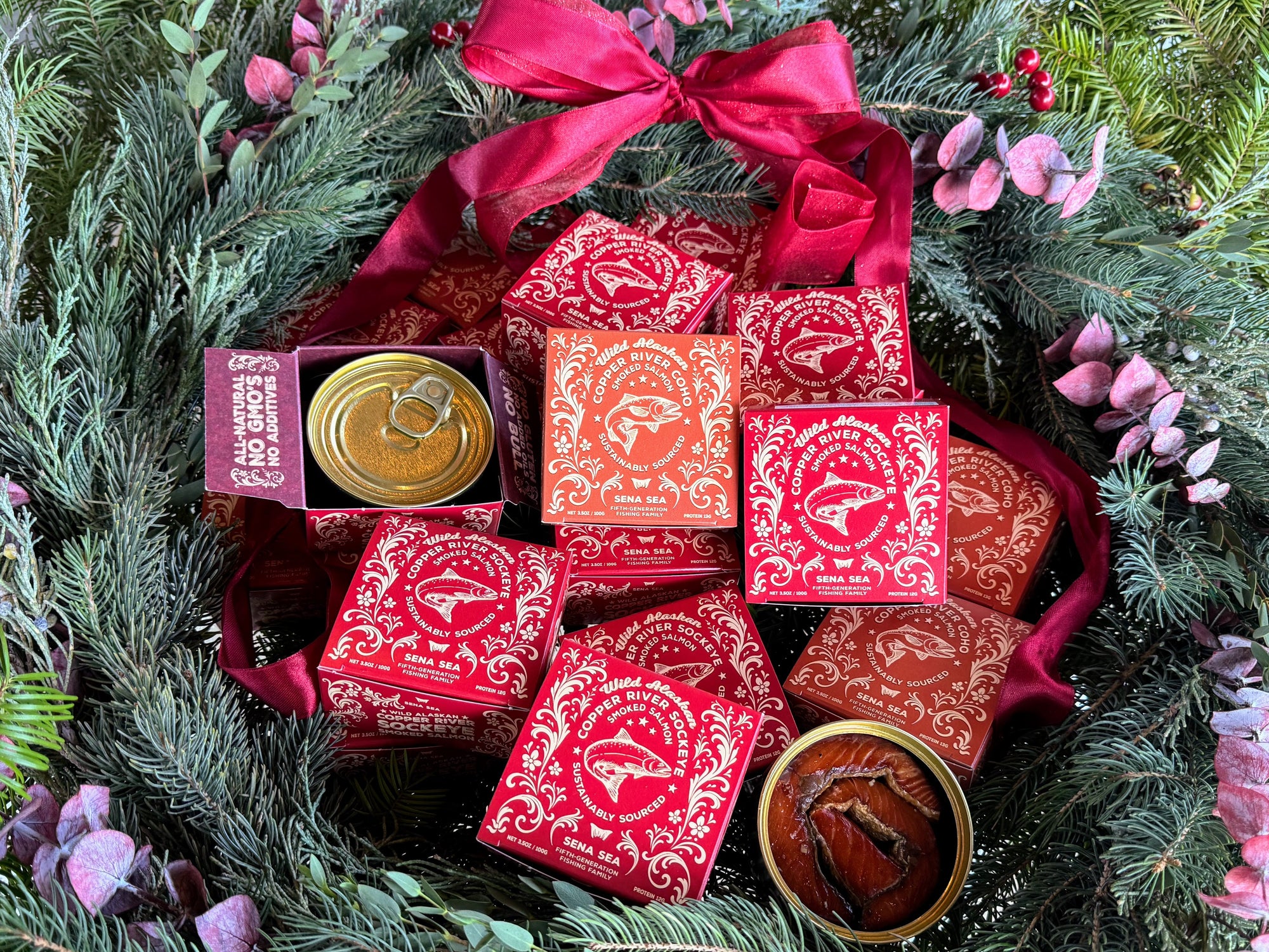 Decorative wreath with red boxes of copper river smoked salmon and pink ribbons on a green leafy background