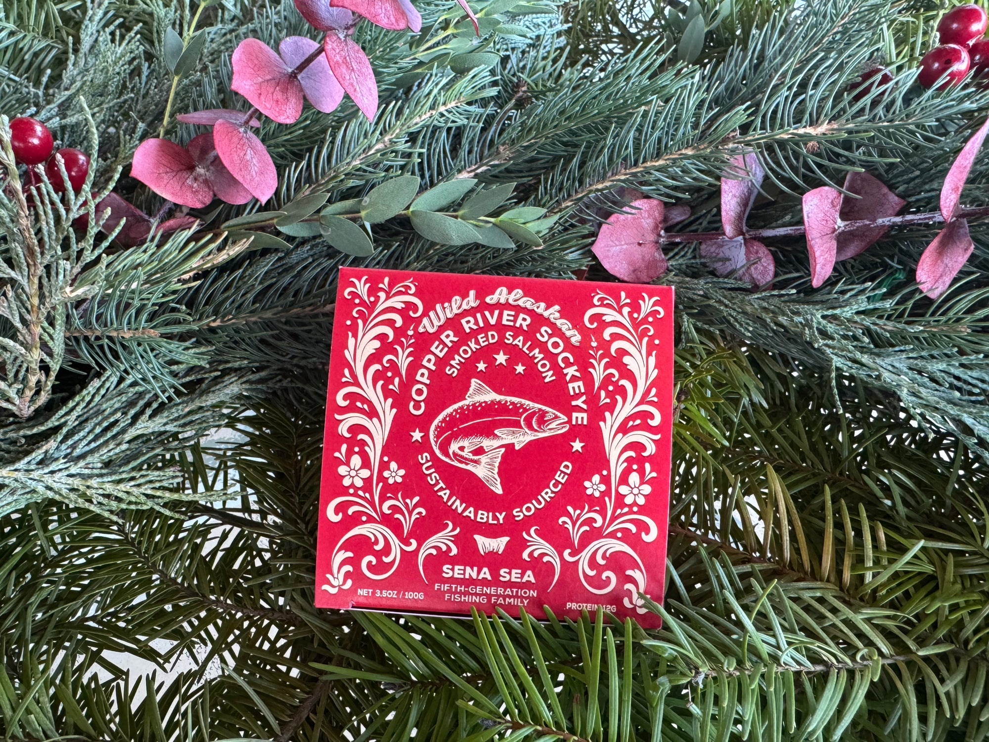 Red smoked Copper River sockeye salmon packaging with white design on a green leafy background