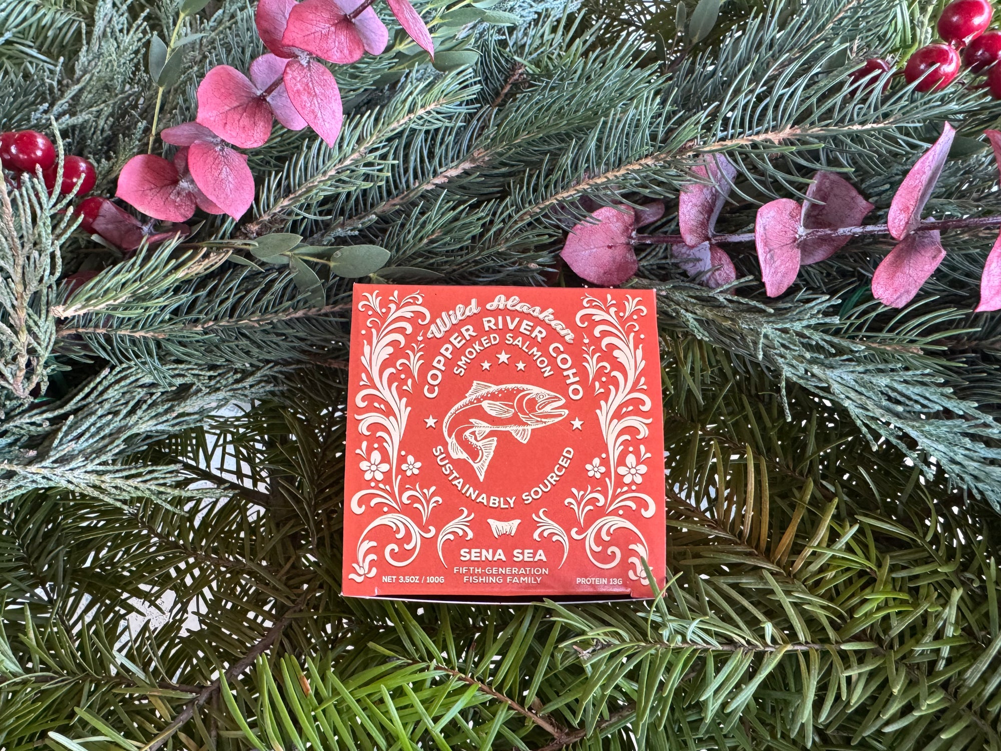 Orange box of smoked Copper River coho salmon 
with white design on a green leafy background