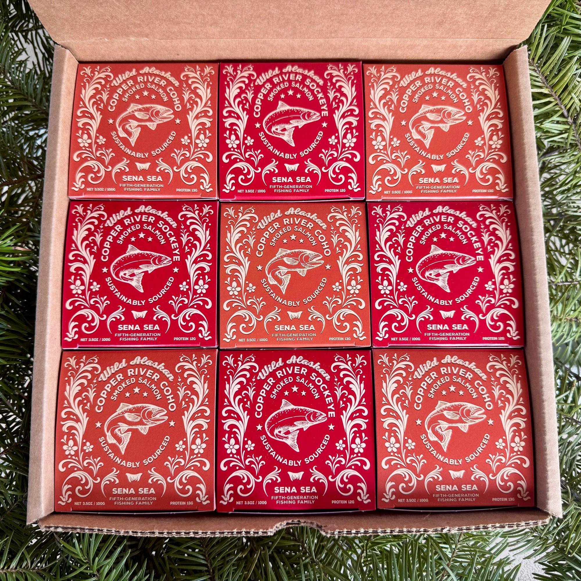 Box of smoked copper river salmon in red boxes with fish design on a green leafy background