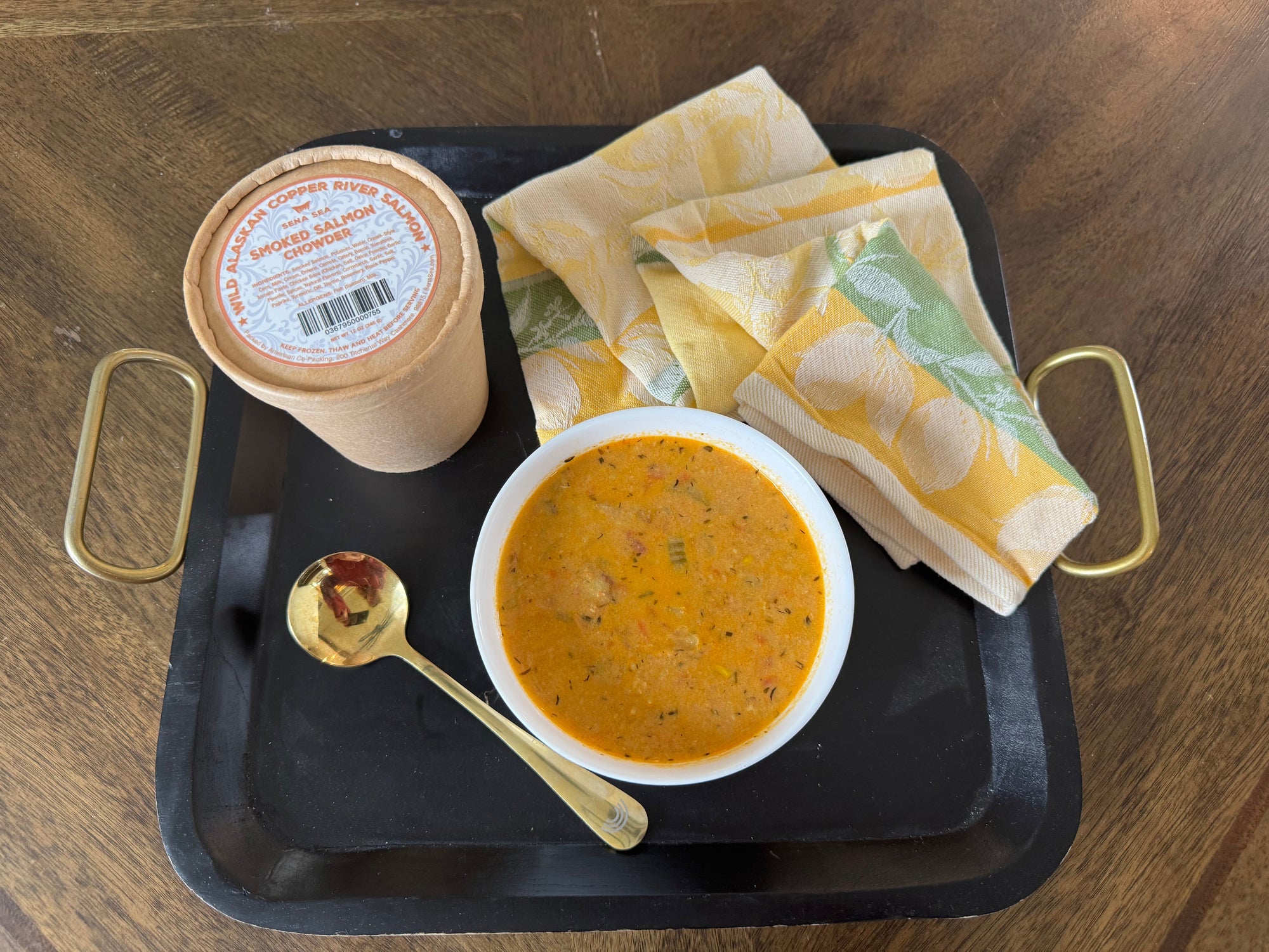 Tray with smoked salmon chowder and a sppon on a wooden surface