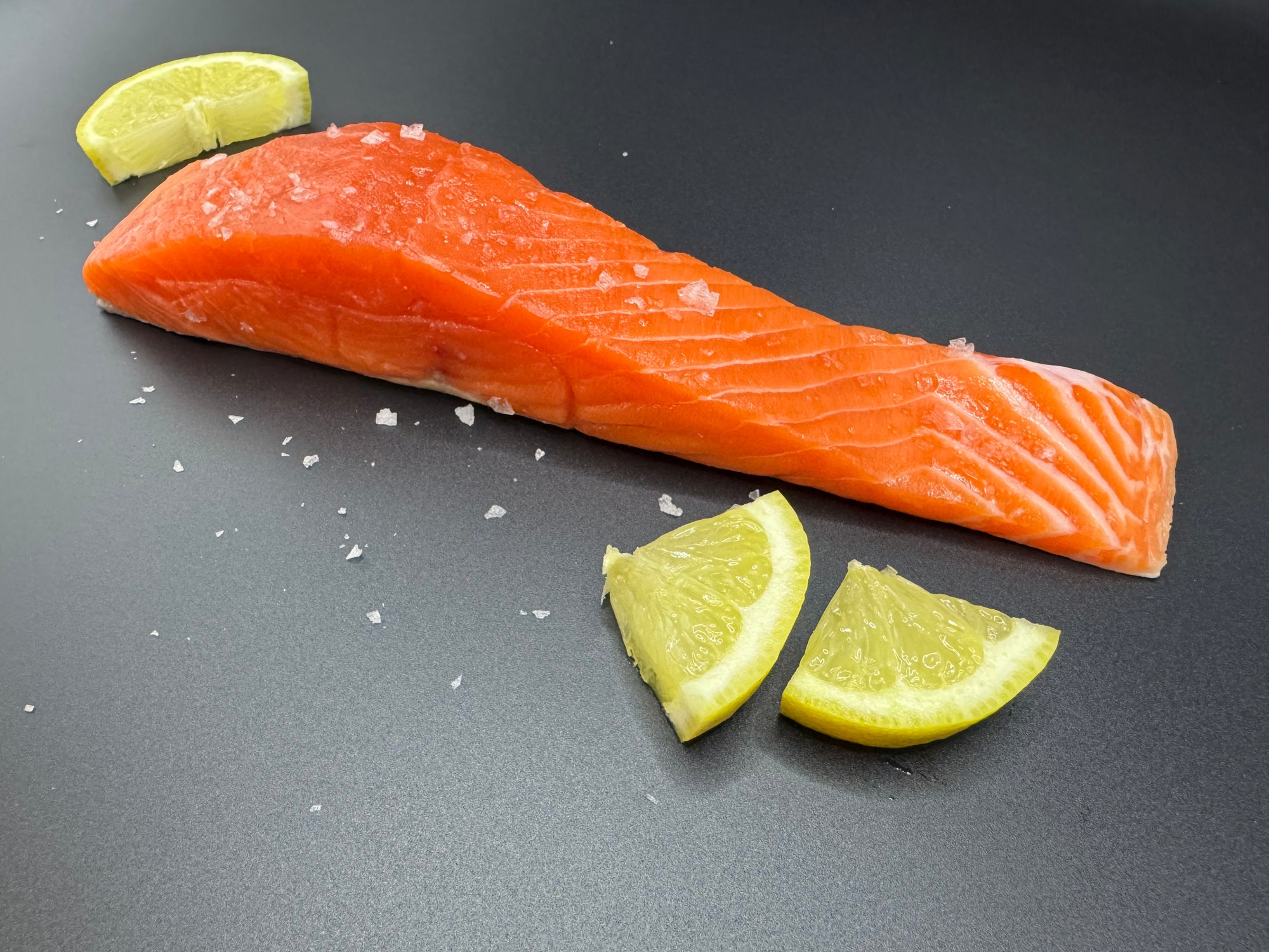 Raw salmon fillet with lemon wedges on a dark surface