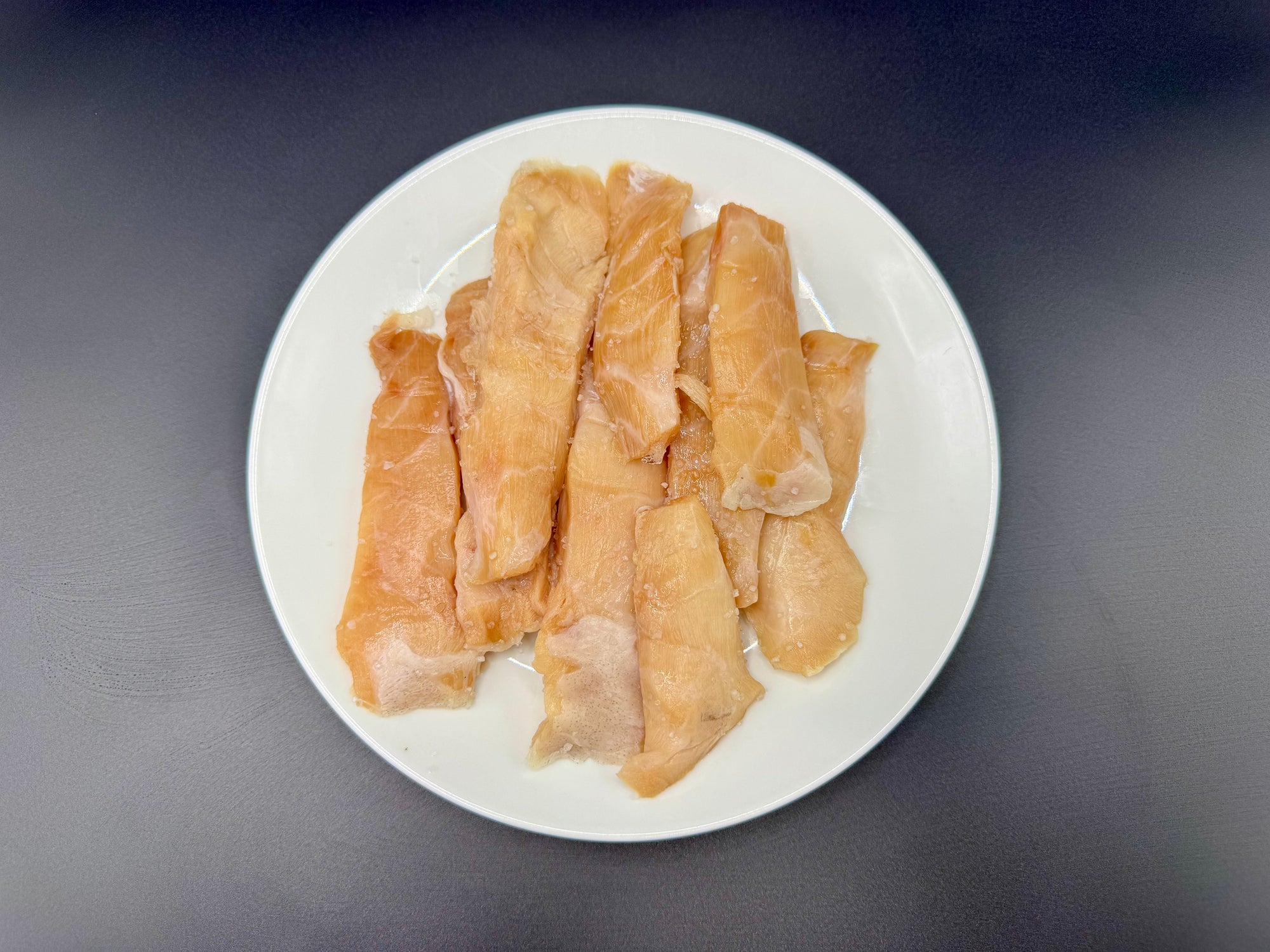 Several Sablefish tips arranged on a white plate, photographed from above on a dark gray surface.