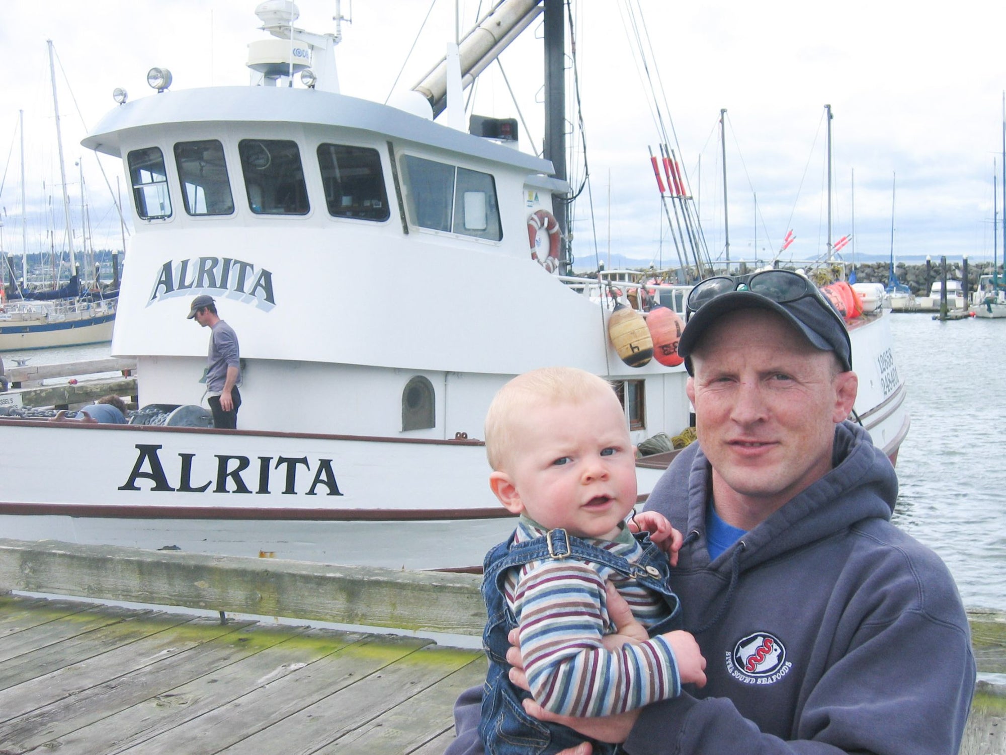 Rich Wheeler, standing in front of the Alrita fishing boat holding baby Hugh